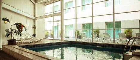A swimming pool with lounge chairs and potted plants, surrounded by large windows.
