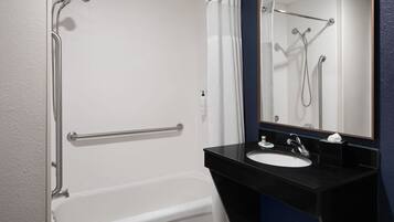 A bathroom with a white bathtub, a black sink, and a mirror.