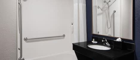 A bathroom with a white bathtub, a black sink, and a mirror.