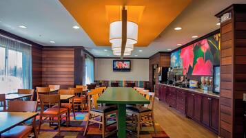 Un restaurante con una mesa verde, sillas de madera y una alfombra colorida.