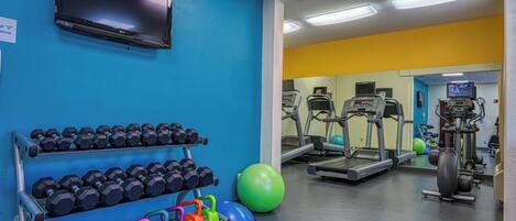 Un gimnasio con equipo de ejercicio, un televisor y un estante con mancuernas.
