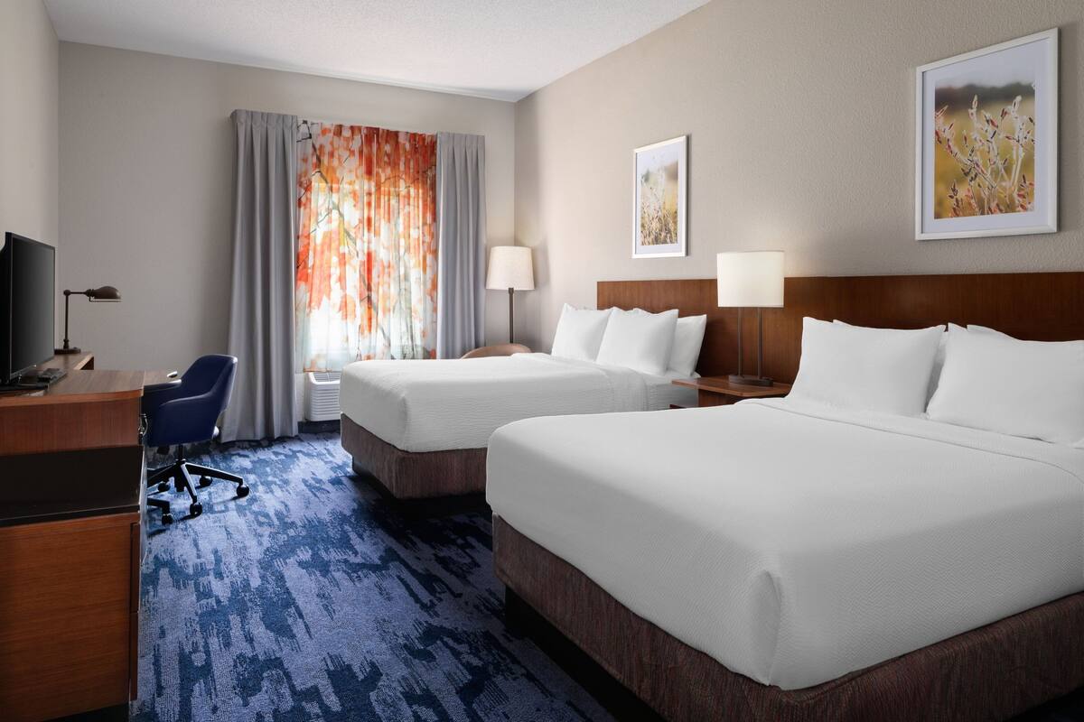 Une chambre d’hôtel avec deux lits, un bureau, une chaise et un téléviseur.