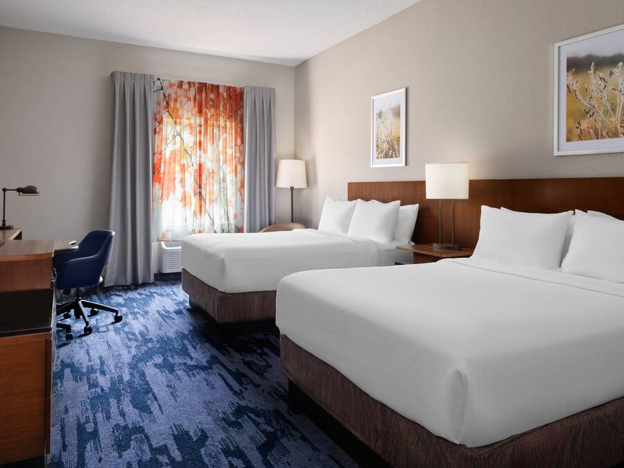 A hotel room with two beds, a desk, a chair, and a TV.