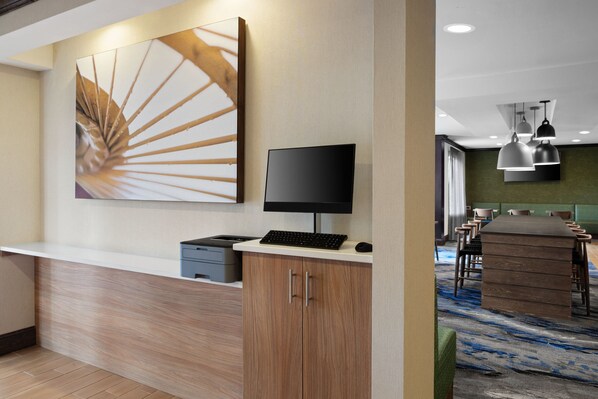 Un moderno vestíbulo de hotel con mostrador de recepción, un cuadro abstracto grande, un televisor de pantalla plana y una mesa de conferencias con sillas.