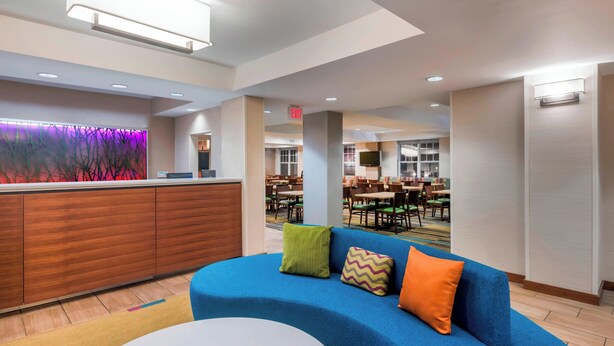 A modern lobby with a blue sofa, a white round table, and a reception desk with a purple-lit wall.