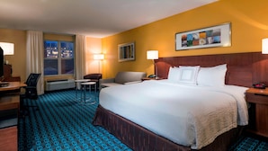 A hotel room with a large bed, a desk, a chair, a small table, and a window with curtains.