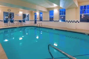 Una piscina interior con agua azul cristalina, un reloj en la pared y un letrero que indica "NO HAY SOCORRISTAS DE GUARDIA".