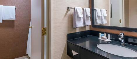 Un baño con un lavamanos negro, un espejo y un perchero con varias toallas.