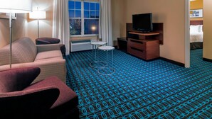 A hotel room with a sofa, armchair, TV, and a patterned carpet.