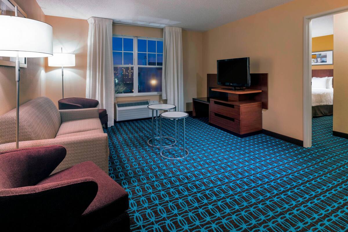 Ein Hotelzimmer mit Sofa, Sesseln, Fernseher und einem gemusterten Teppich.
