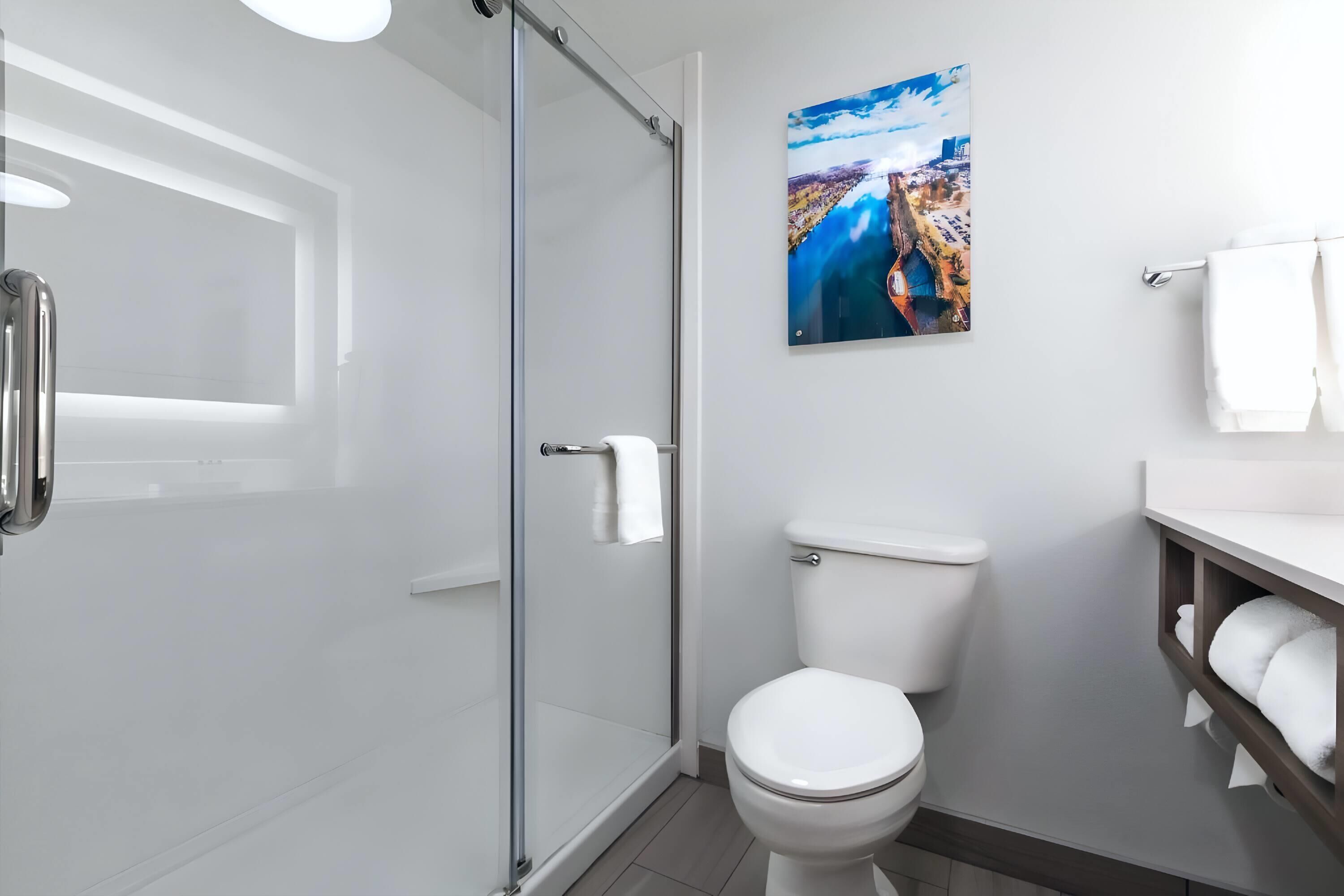 Un baño moderno con cabina de ducha de vidrio, inodoro blanco y lavamanos adosado a la pared con toallero.