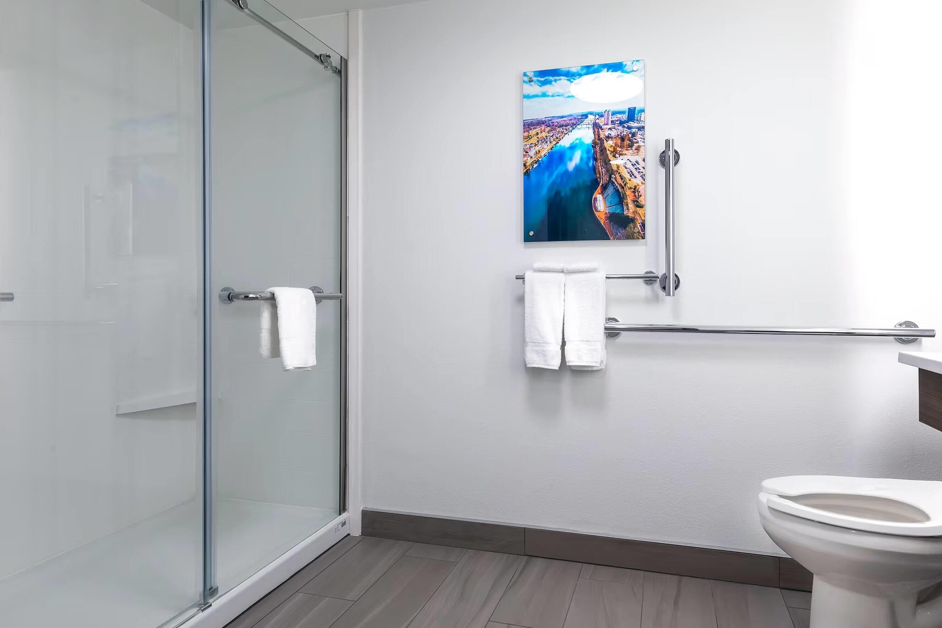 Une salle de bain moderne avec une douche à parois de verre, des toilettes blanches et un porte-serviettes fixé au mur.