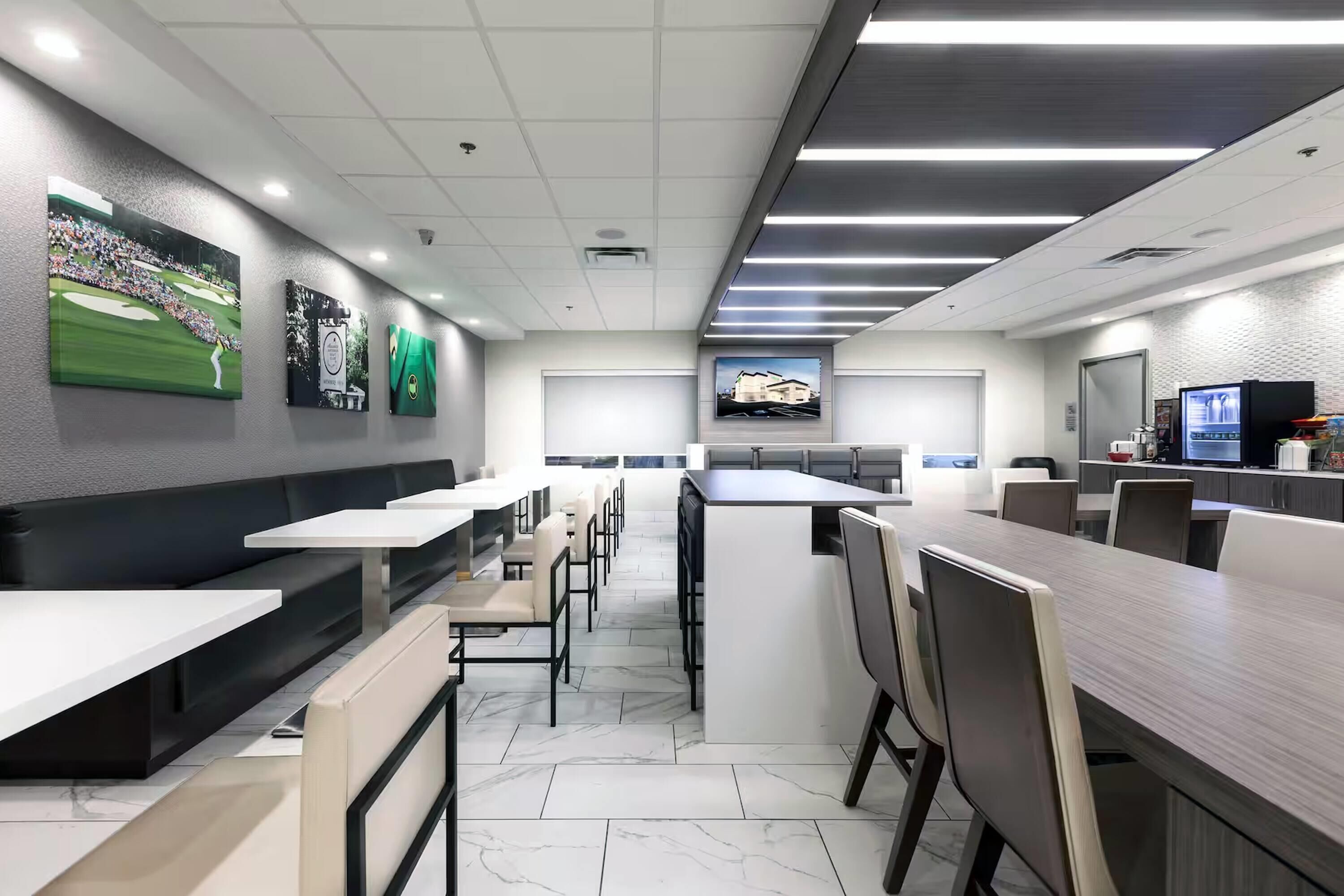 Un restaurante moderno con mesas comunitarias largas y cabinas, además de una zona de cocina y una pantalla de televisión.