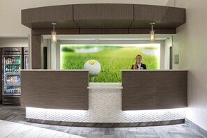 A reception desk with a golf ball in the background, a refrigerator with beverages, and a check-in counter. - Wingate by Wyndham Augusta Washington Road (Augusta)