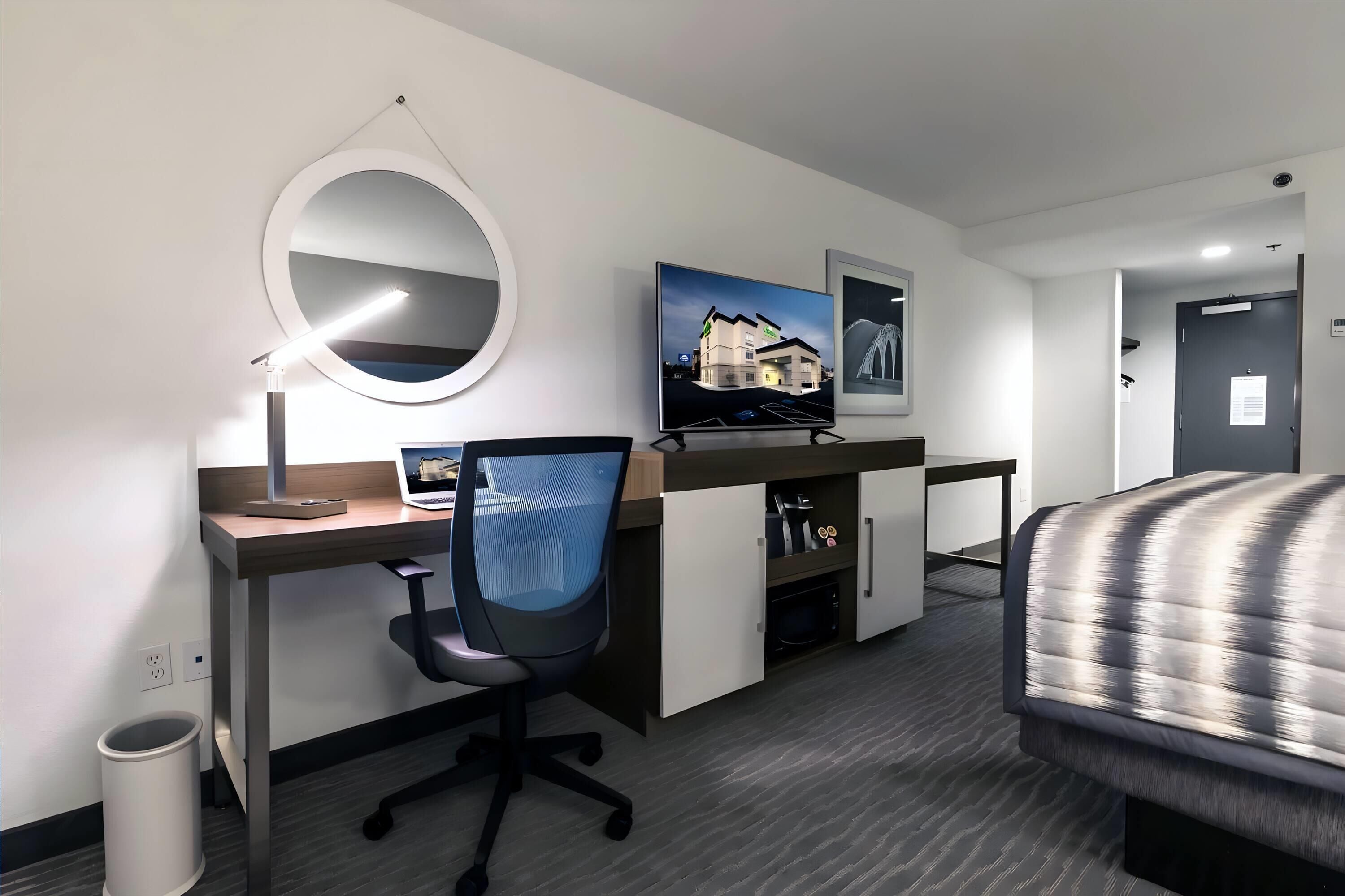 Habitación de hotel con escritorio, silla, cama, televisor y un espejo grande.