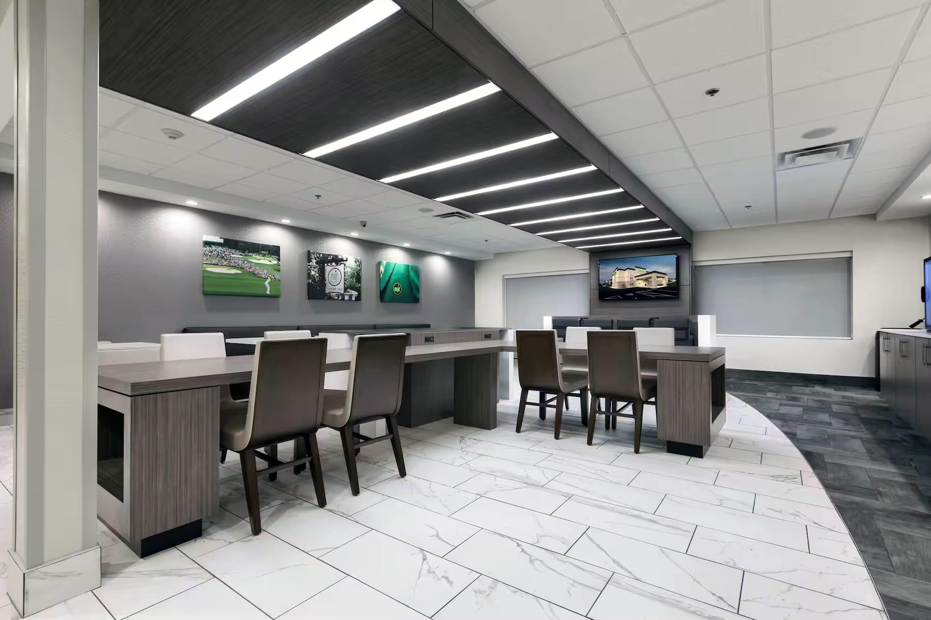 A modern office space with a long counter, multiple chairs, and a large screen displaying a golf course.