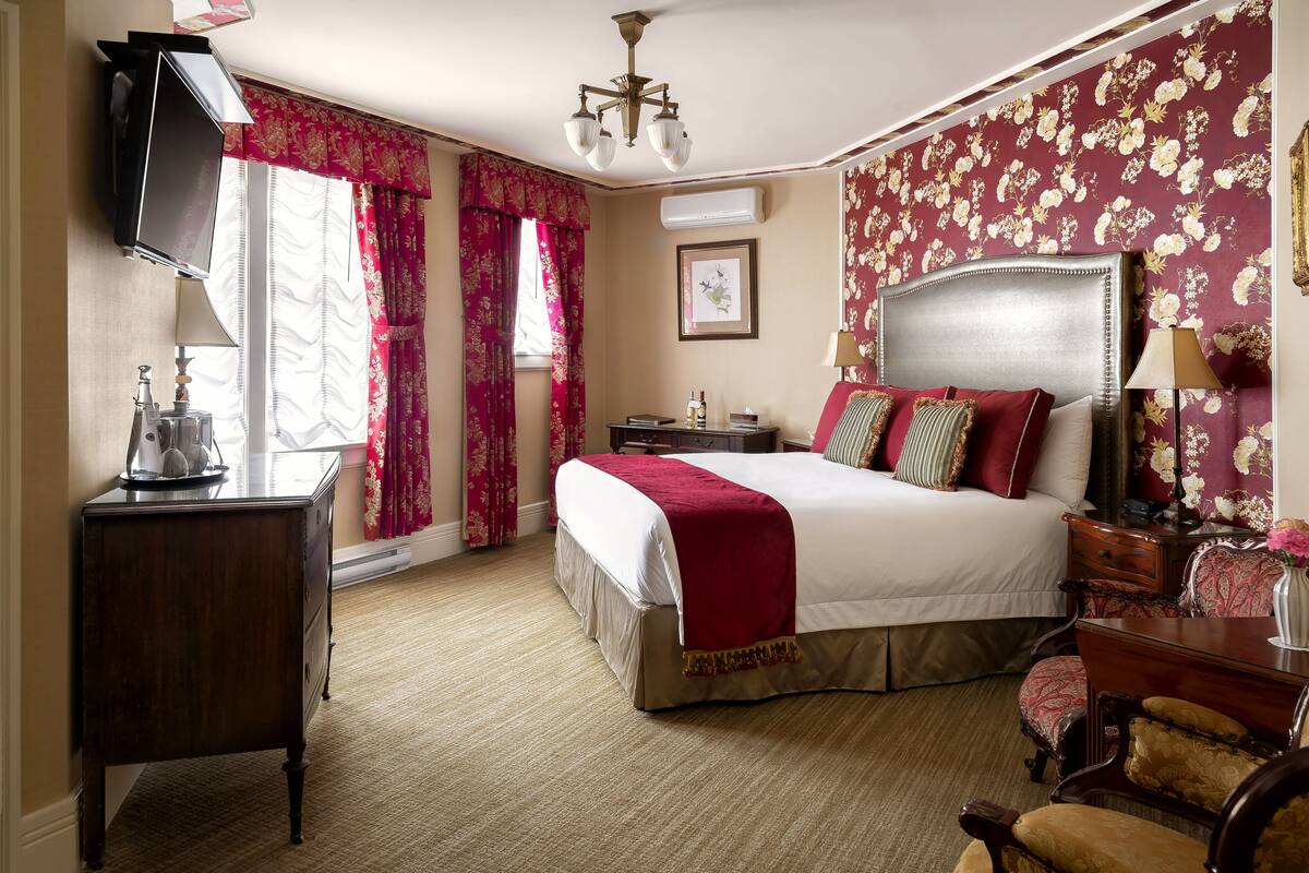 Habitación de hotel con cama, escritorio, silla, televisión y ventana con cortinas.