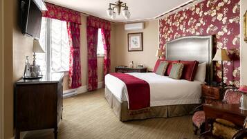 A hotel room with a bed, a desk, a chair, a television, and a window with curtains.