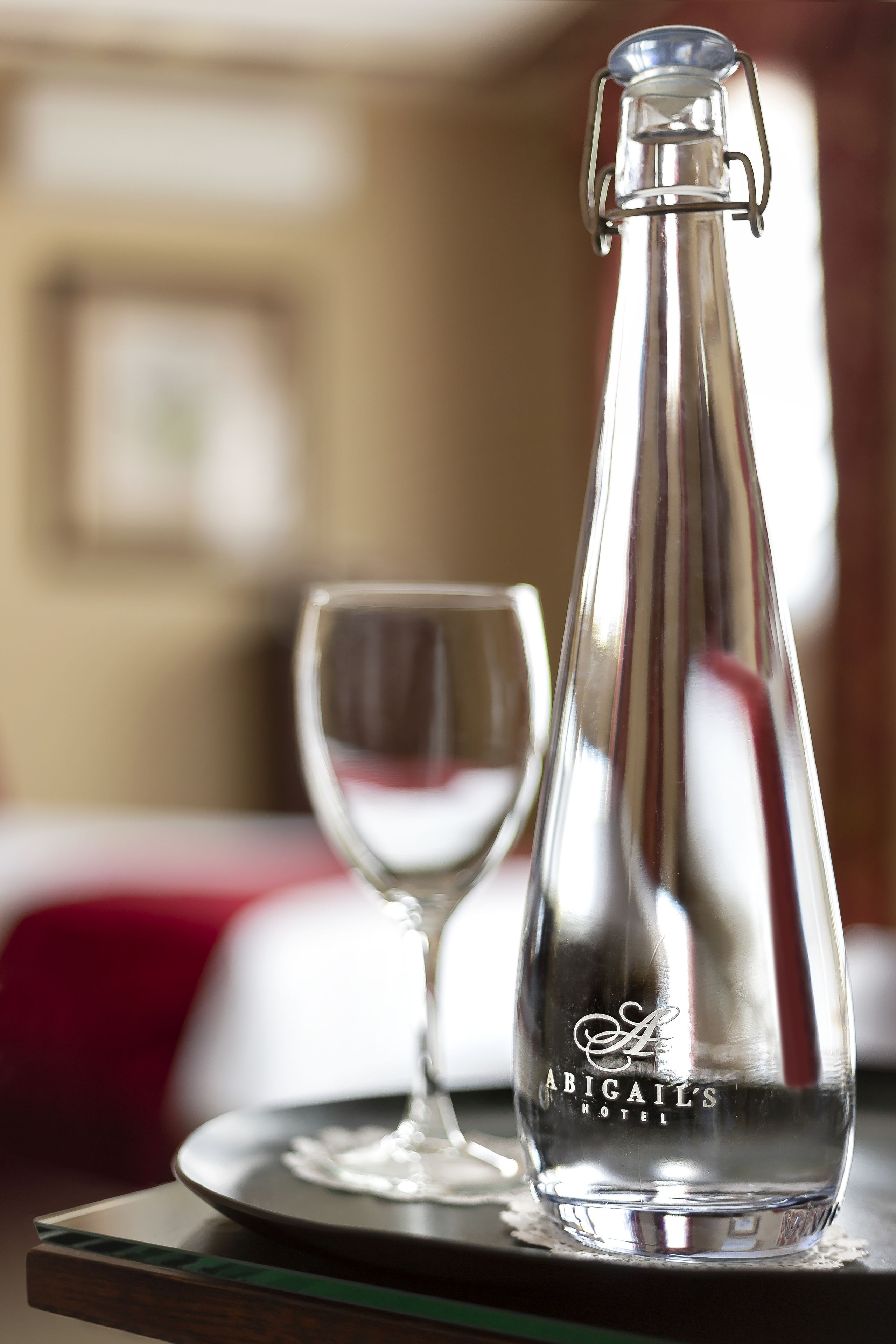 A clear glass bottle with a metal clasp and a glass on a tray.