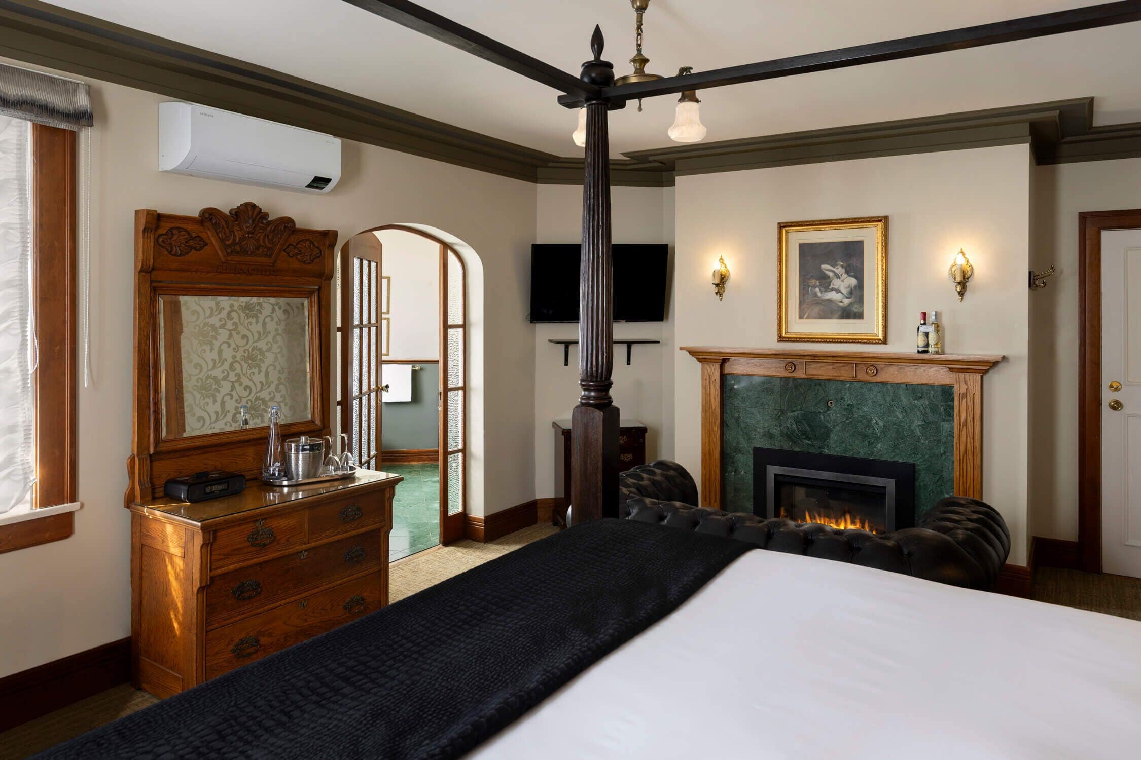Une chambre d’hôtel avec un grand lit, une commode en bois, une cheminée et un téléviseur fixé au mur.
