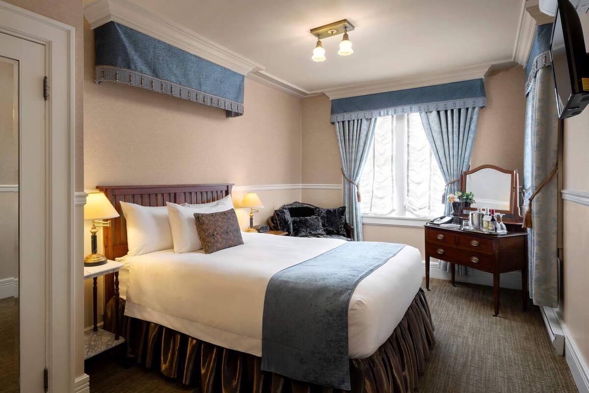Habitación de hotel con una cama grande, cómoda, espejo y ventana con cortinas.