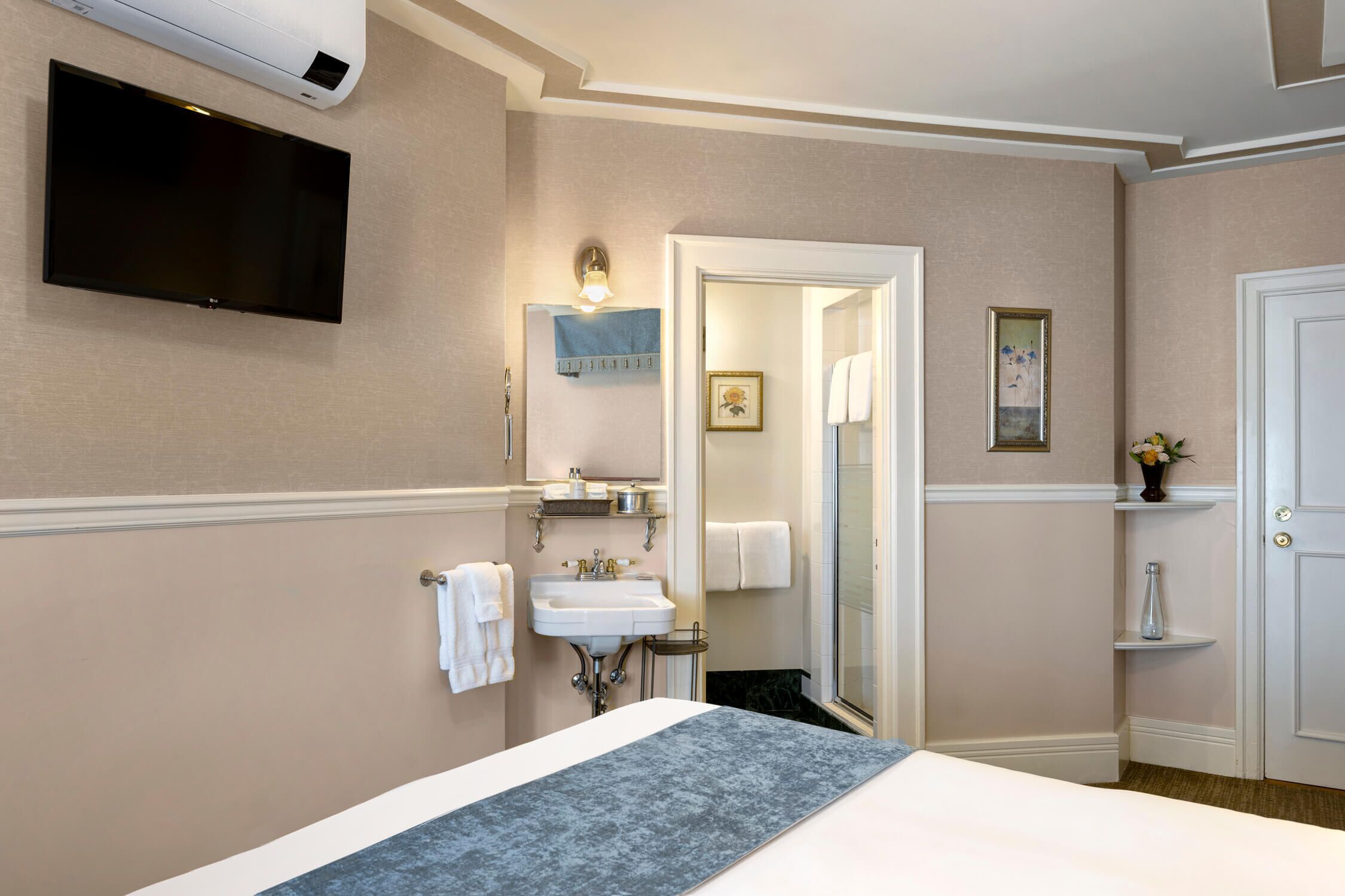 A hotel room with a bed, a flat-screen TV mounted on the wall, a sink, and a mirror.