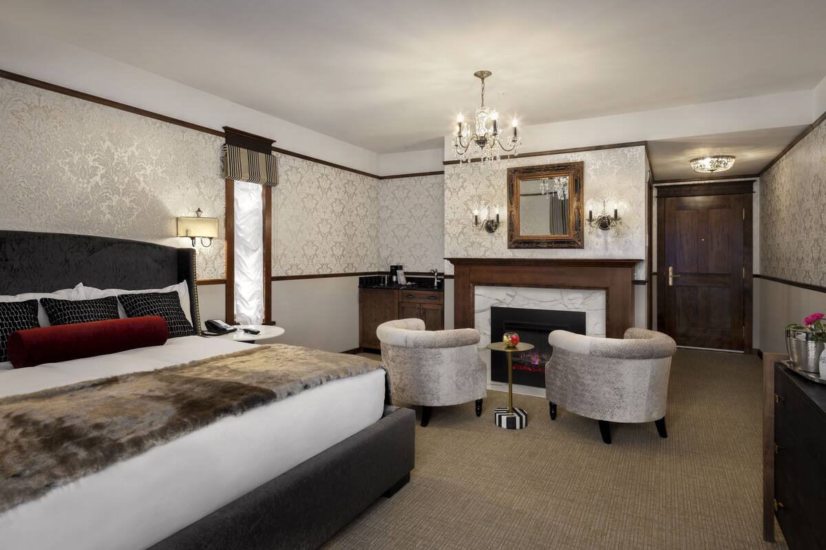 Habitación de hotel con una cama grande, dos sillones, una mesita con un florero, una chimenea y un espejo sobre ella.