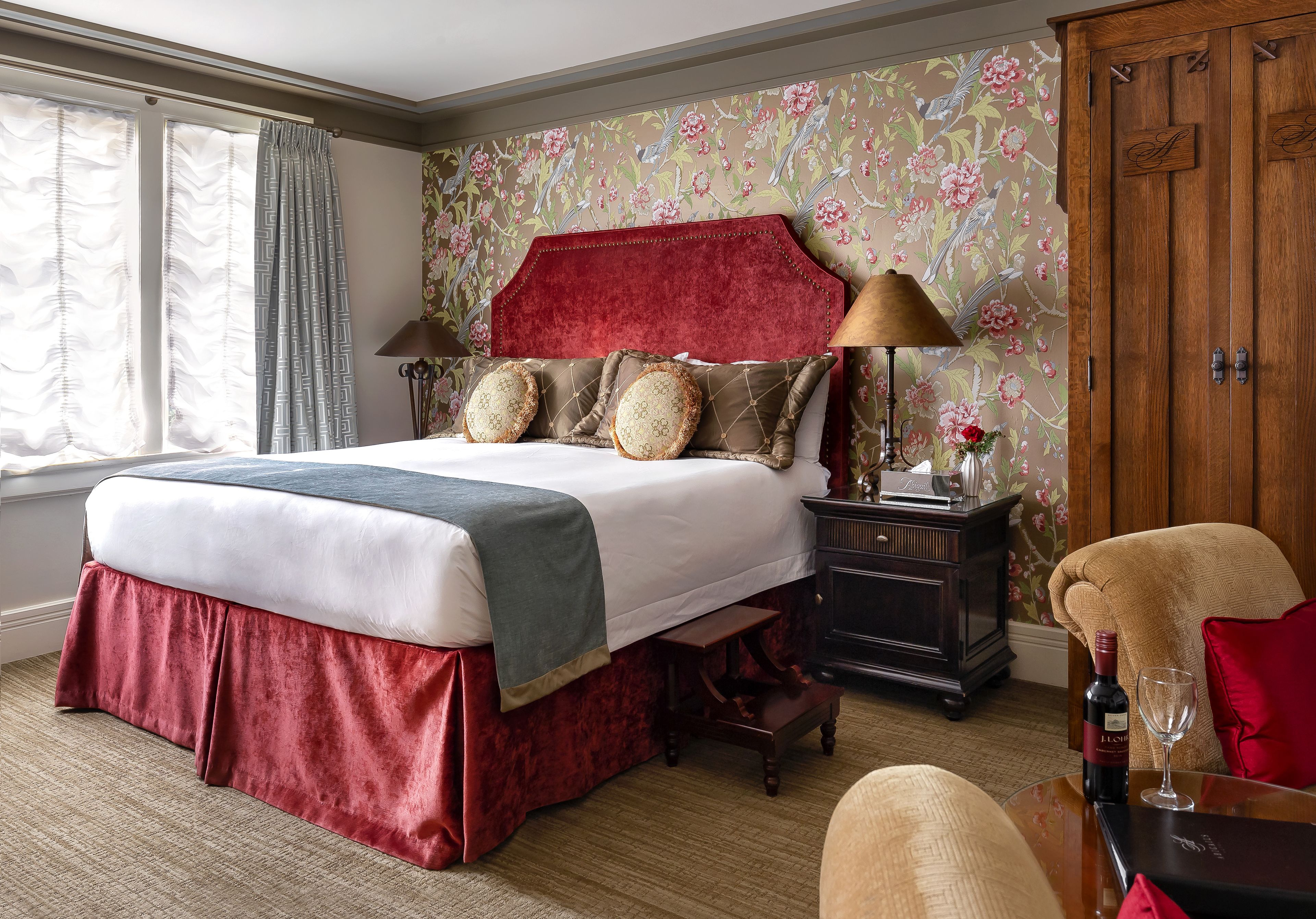 Une chambre d’hôtel avec un grand lit, une armoire en bois, un bureau avec une lampe et une fenêtre avec des rideaux.