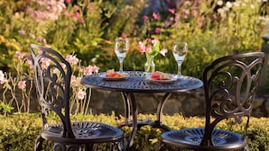 A round metal table with two chairs, each with a plate of food and a glass of water, set in a garden with pink flowers. - Abigail's Hotel (Victoria)