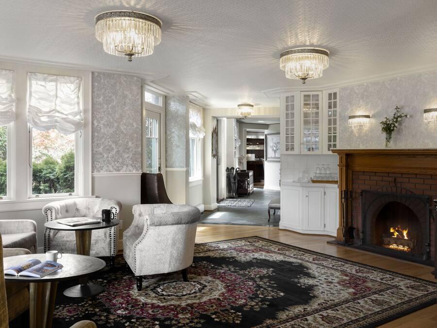 A spacious living room with a fireplace, elegant chandeliers, and a large window with curtains.