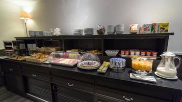 A buffet setup with various food items and containers, including a coffee maker and cereal boxes.