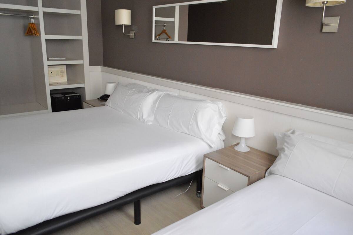 A hotel room with two beds, a wardrobe, a bedside table with a lamp, and a mirror on the wall.