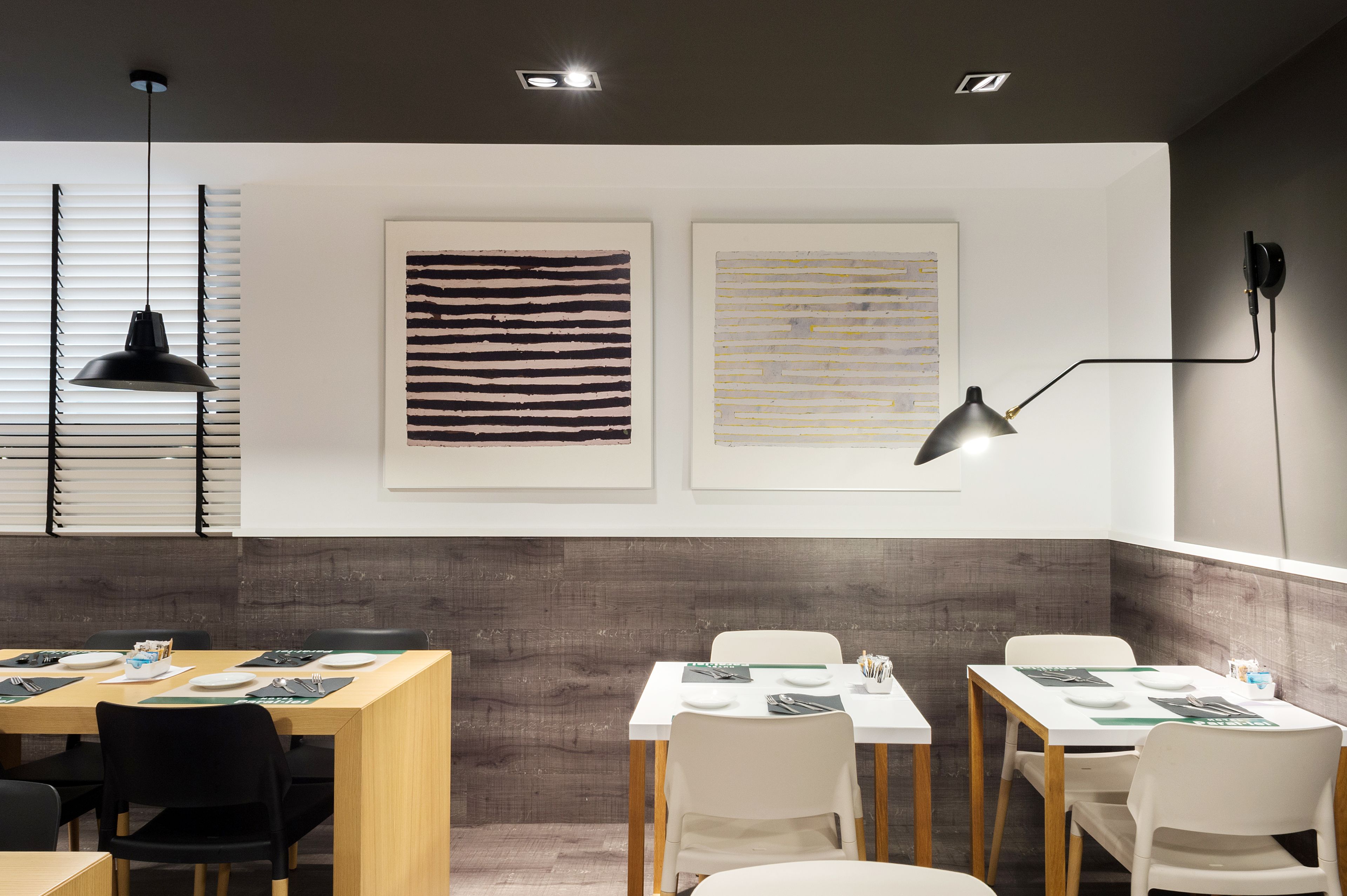 A modern dining area with tables set for meals, overhead lighting, and artwork on the walls.