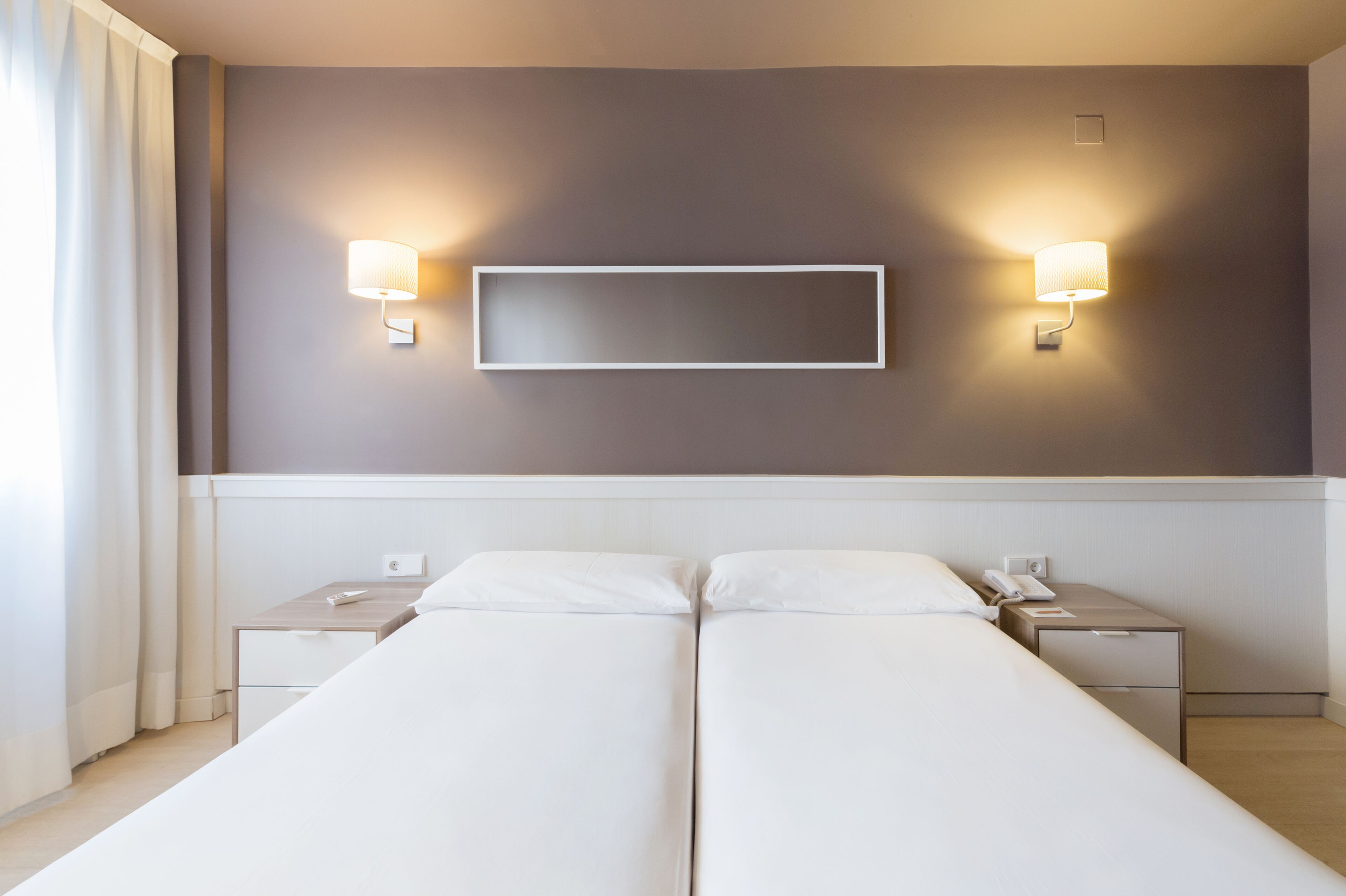 A hotel room with a double bed, two bedside tables, a mounted TV, and wall-mounted lamps.