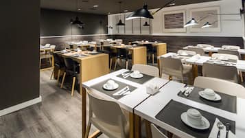 A modern dining area with multiple tables and chairs, equipped with black table lamps and a neutral color scheme.