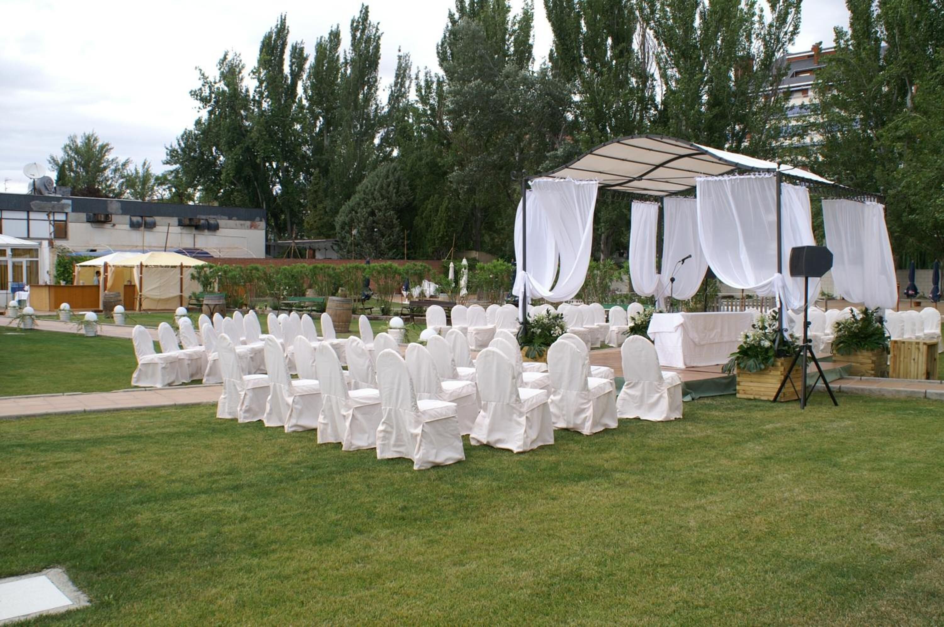 Een evenemententerrein buiten, met rijen witbedekte stoelen en een tent met witte gordijnen.