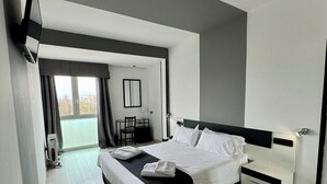 Una habitación de hotel moderna con una cama grande, una mesita de noche, un escritorio con una silla y vistas a la ciudad por la ventana.