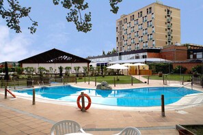 Un hotel con piscina, mobiliario exterior y un edificio grande al fondo.
