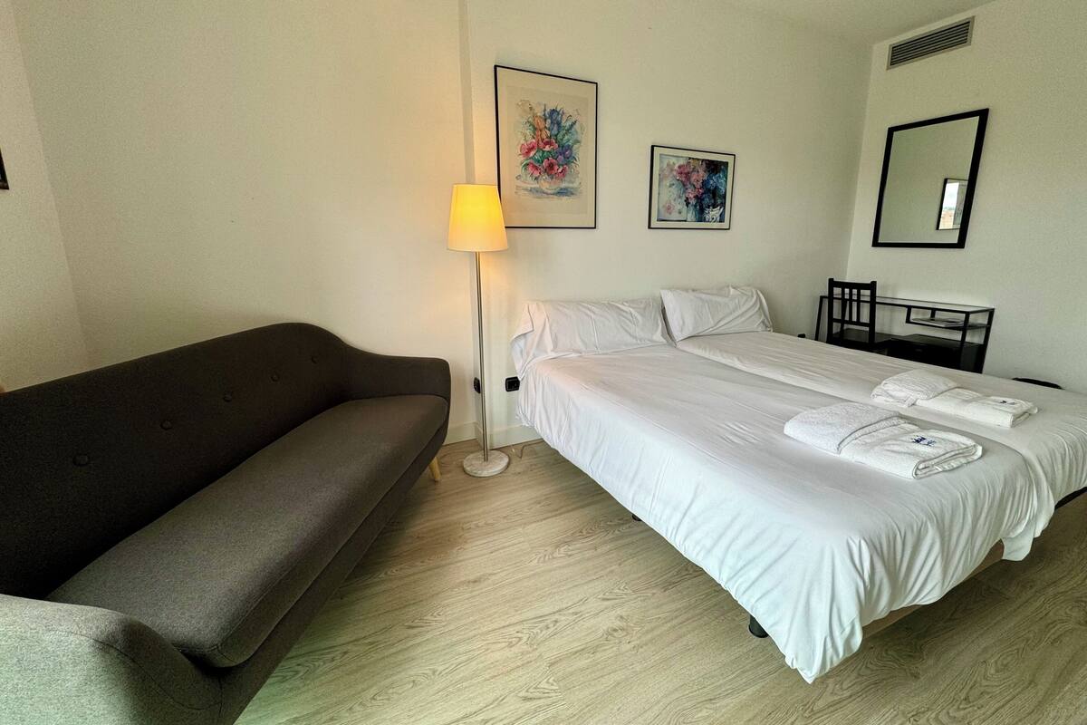 A hotel room with a bed, a sofa, a desk, and a lamp.