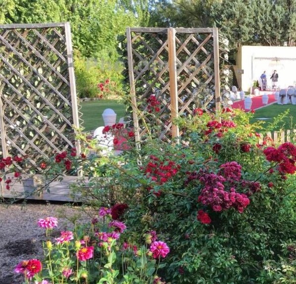 Un jardín con valla de madera, una estatua blanca y una mesa cubierta con mantel rojo.