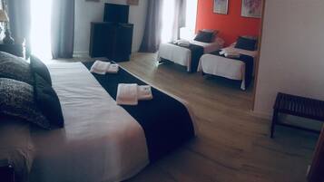 A hotel room with two beds, a bench, a TV, and a desk.