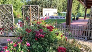 Un jardín con un porche de madera, un escenario con sillas y un área cercada.