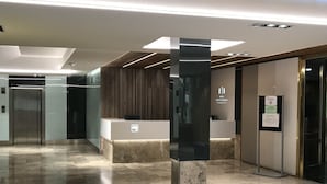 Een moderne hotellobby met een receptiebalie, een zwarte kolom en een lift.