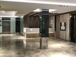 Un moderno vestíbulo de hotel con mostrador de recepción, una columna negra vertical y un ascensor.