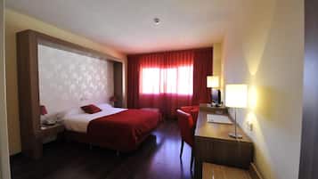 A hotel room with two beds, a desk, a chair, a desk lamp, and a window with red curtains.