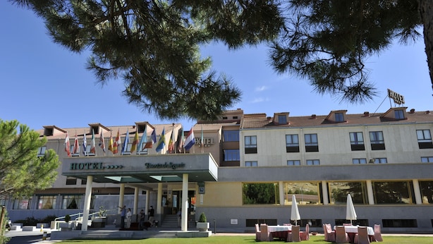 Een hotel met een overdekte ingang, terras en verschillende vlaggen.