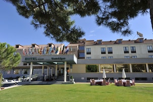 Un hotel con entrada cubierta, mesas al aire libre y varias banderas.