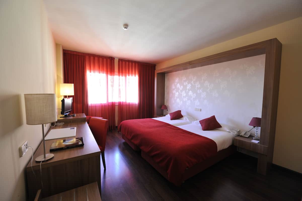 Een hotelkamer met een groot bed, een bureau met een lamp, een stoel en een raam met rode gordijnen.