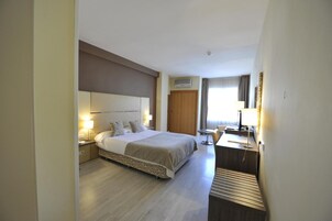 Una habitación de hotel con una cama grande, mesitas de noche, un escritorio y una silla.