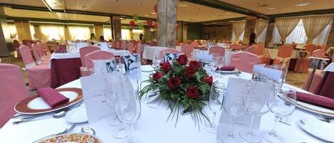 A banquet hall with round tables set for dining, featuring red roses and white tablecloths.